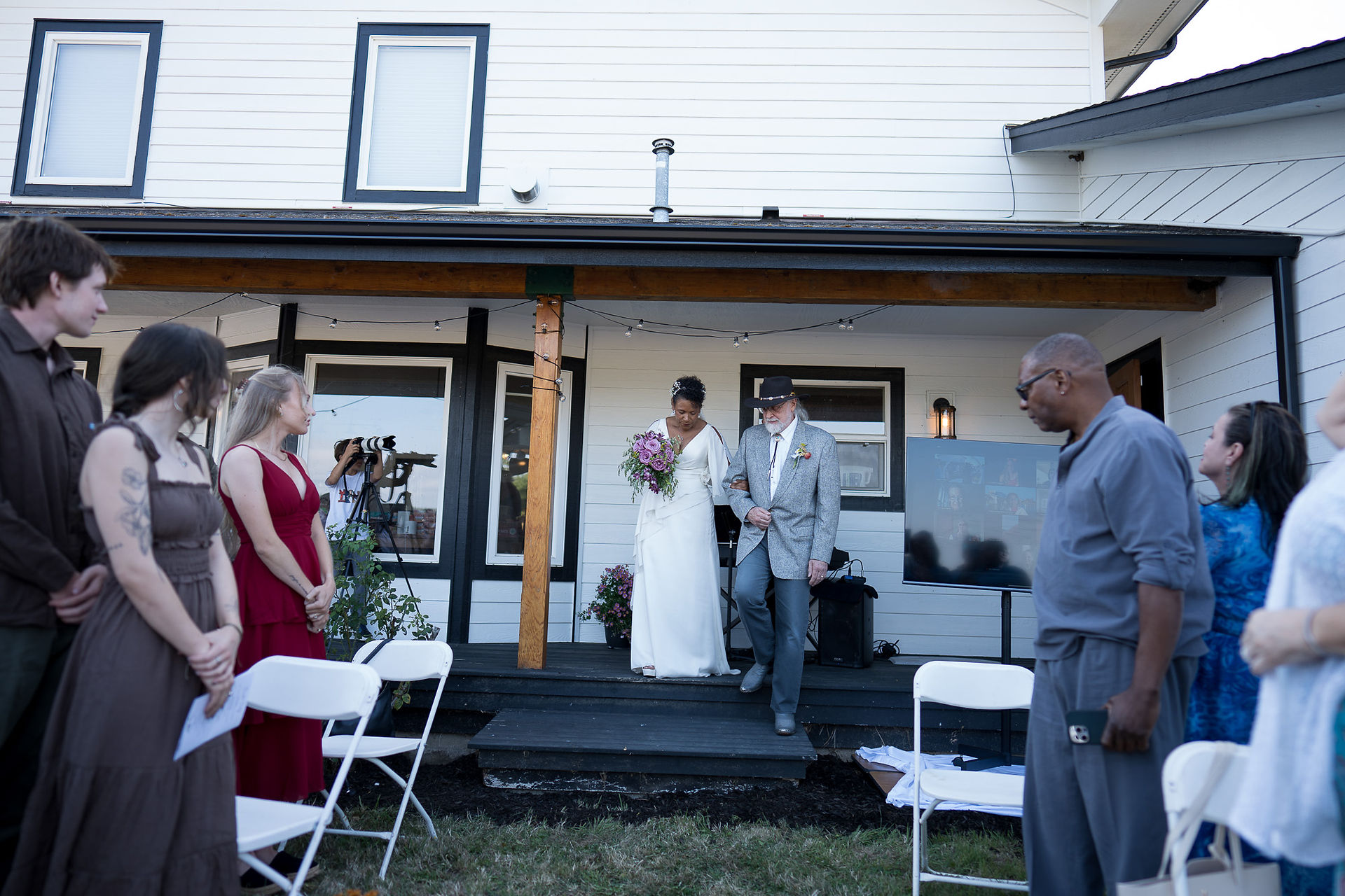 Bride in white dress walks down steps with man for wedding.