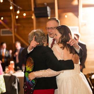 Man hugs bride and woman at rustic wedding reception.