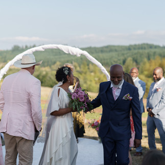 Bride and man walk during intimate outdoor farm wedding ceremony.