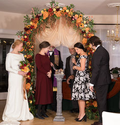 Bride and guests at fall wedding ceremony under vibrant floral arch.