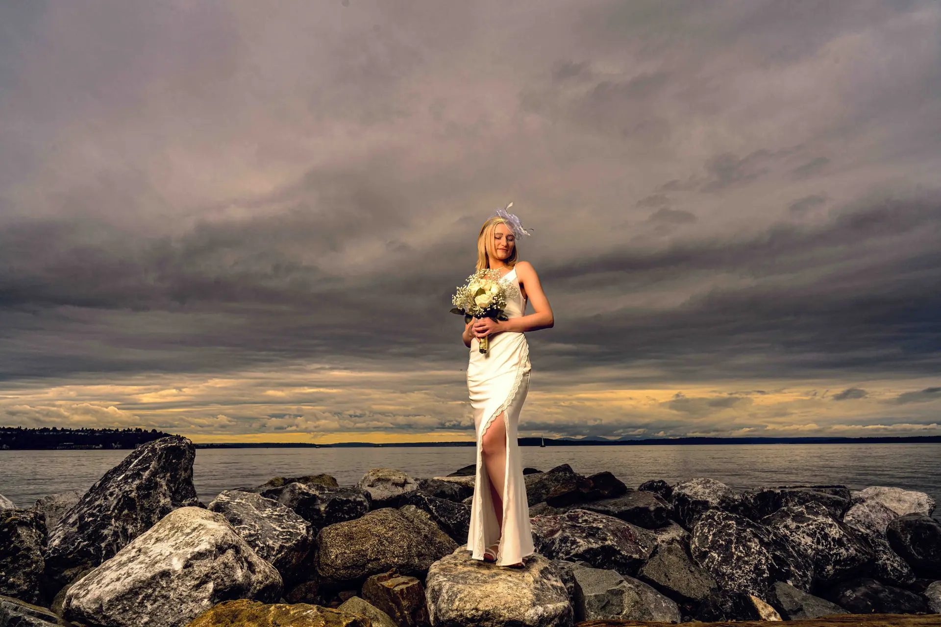 Bride in white gown, bouquet, ocean rocks