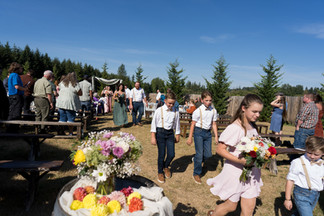 Children walk with flowers at a sunny outdoor wedding ceremony.