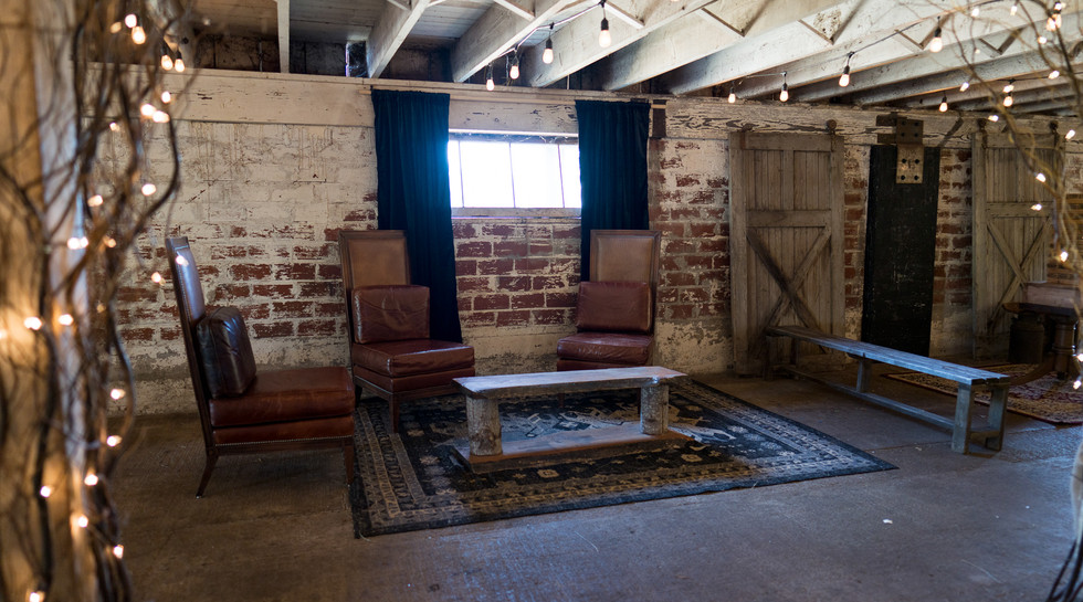 Rustic barn lounge area with leather chairs, coffee table, and string lights.