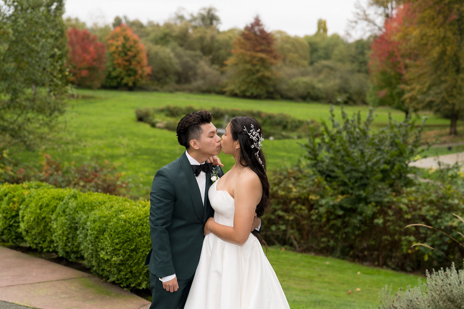 Bride and groom kissing outdoors with vibrant autumn foliage background.