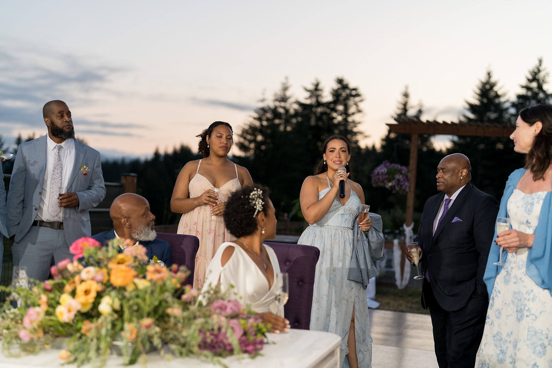 Woman giving speech into microphone at outdoor wedding reception.
