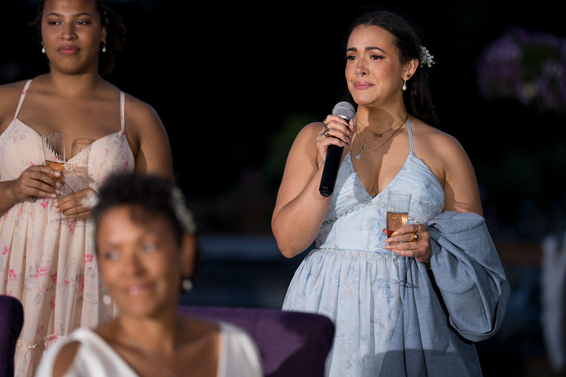 Woman in light blue dress speaking into microphone at evening reception.