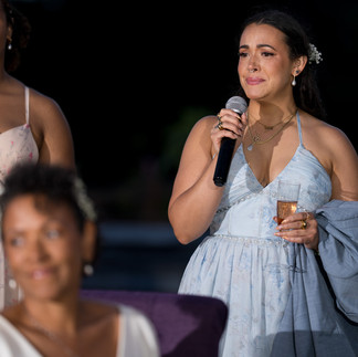 Woman in light blue dress speaking into microphone at evening reception.