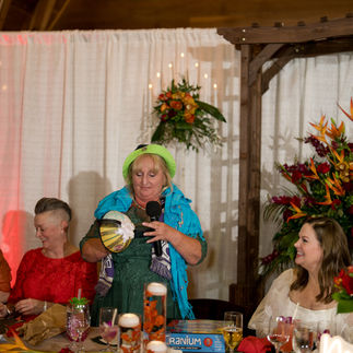 Woman in green hat speaks at a festive wedding reception table.