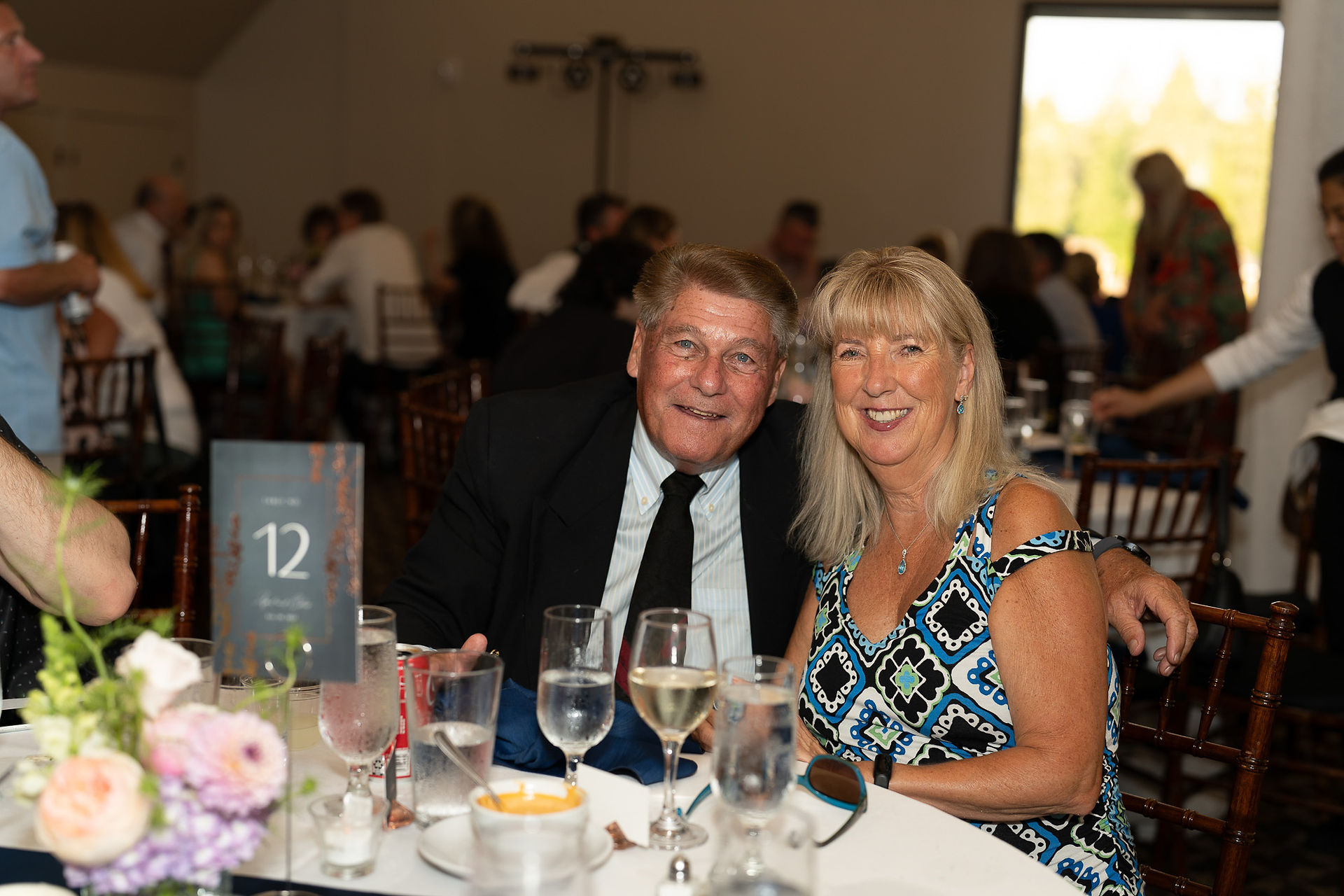 Smiling man and woman at reception table with "12" card.