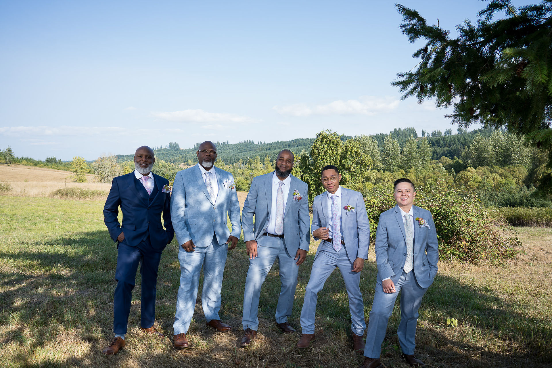 Five men in blue suits posing outdoors with green hills.
