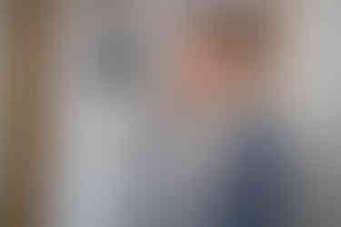 Smiling person in light blue suit, patterned tie, and floral boutonnière.