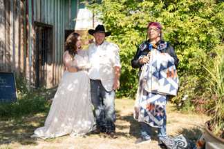 Bride, groom, and man holding quilt at outdoor wedding ceremony.