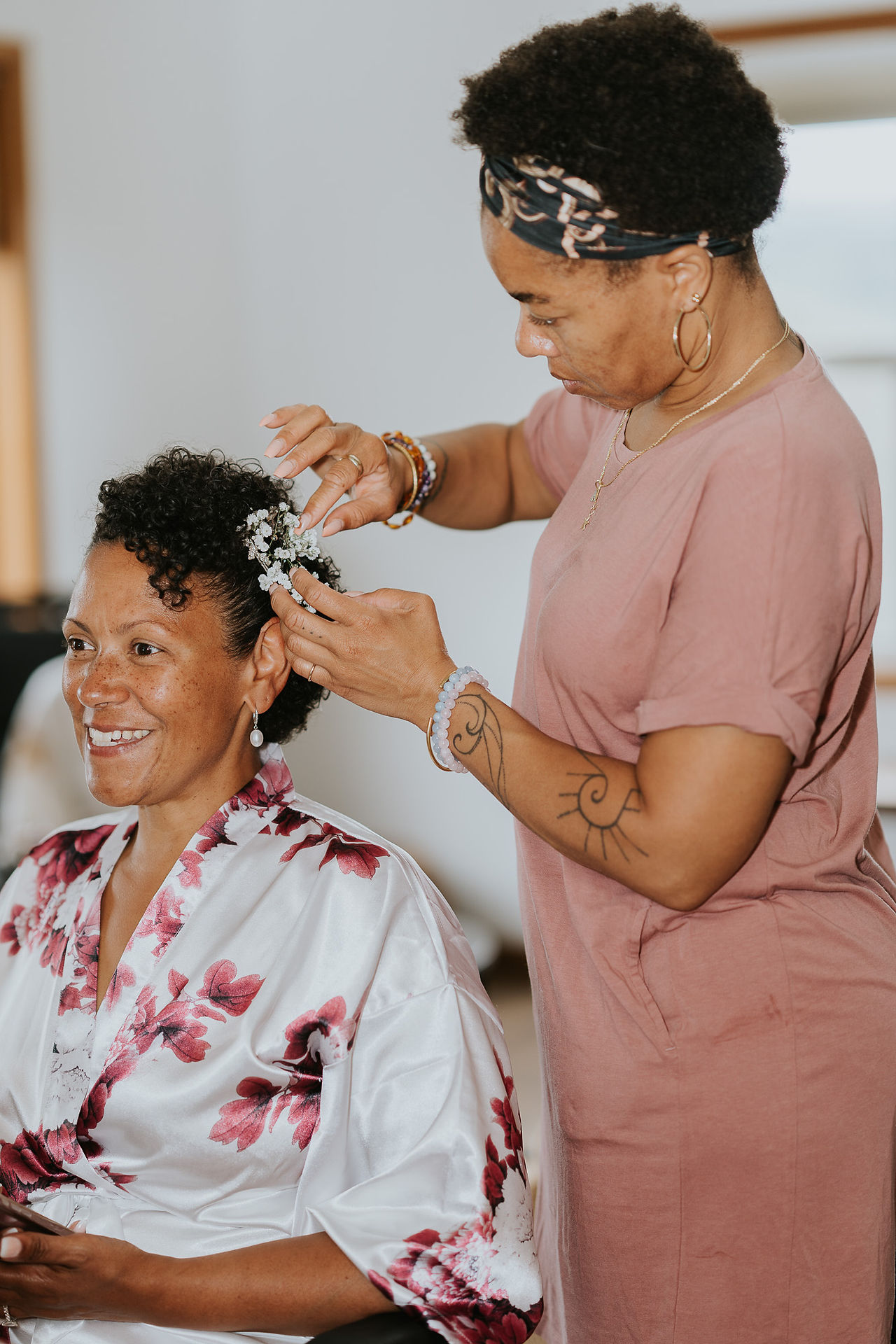 Bride smiling as stylist adds white flowers to her hair.