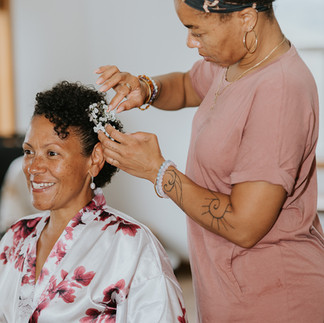 Bride smiling as stylist adds white flowers to her hair.