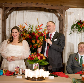 Groom gives speech, bride smiling at their decorated wedding reception table.