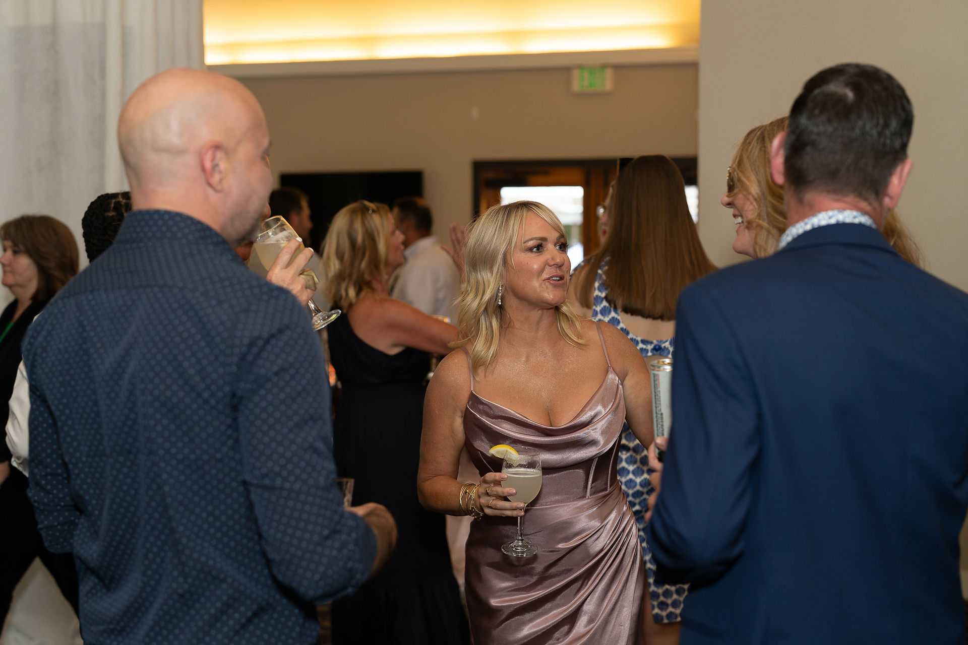 Elegant woman in strapless dress holding cocktail, enjoying wedding reception.