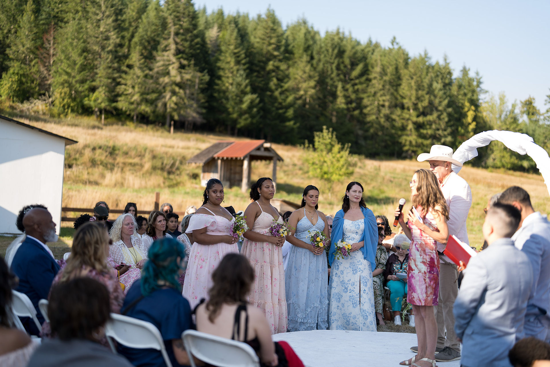 Four bridesmaids in pastel dresses stand outdoors at a farm wedding.