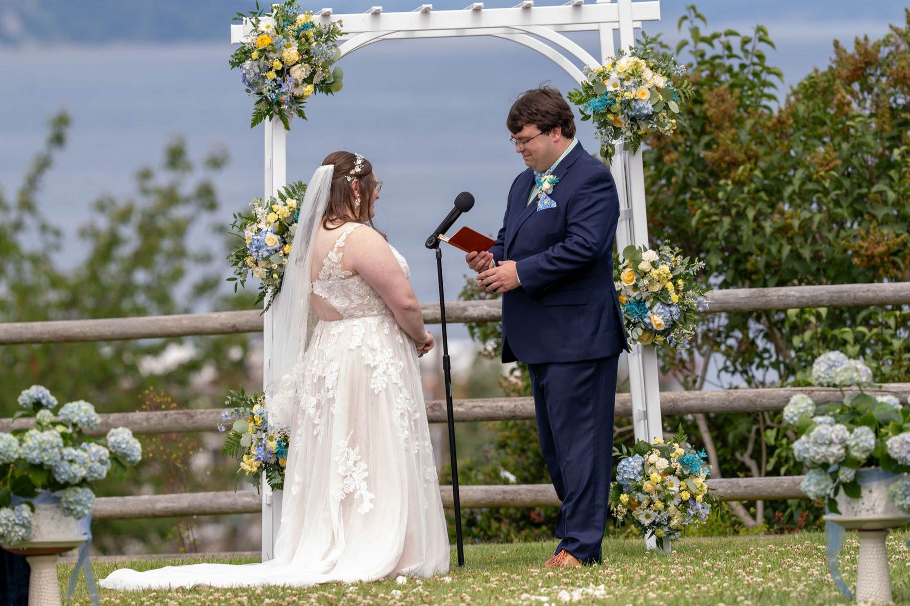 Bride and groom exchanging vows under a floral arbor at outdoor wedding.