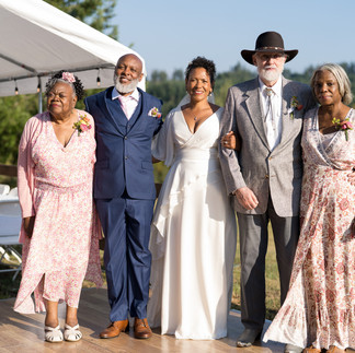 Bride and groom with smiling family members at outdoor farm wedding.
