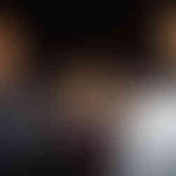 Woman at table looks at camera, under tent with flowers.
