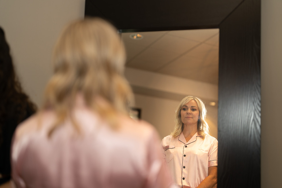Blonde woman in pink pajamas admiring her reflection in a mirror.