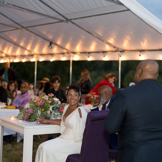 Bride listens intently to speaker at intimate farm wedding reception.