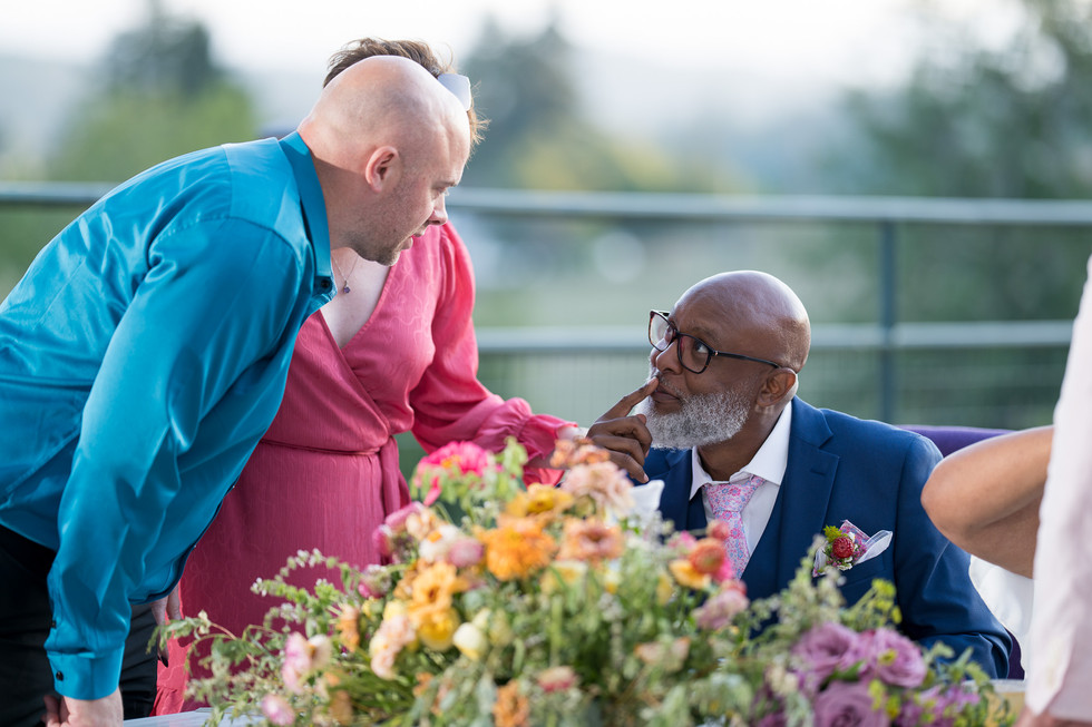 Guest talks to older man in suit listening intently at outdoor wedding.