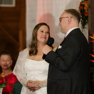 Bride looking at groom speaking into microphone during wedding reception speech.