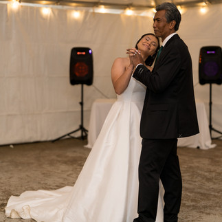 Bride in white gown dancing lovingly with father at reception.
