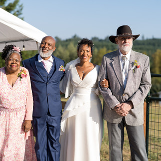 Smiling bride, groom in cowboy hat, and family at intimate farm wedding.