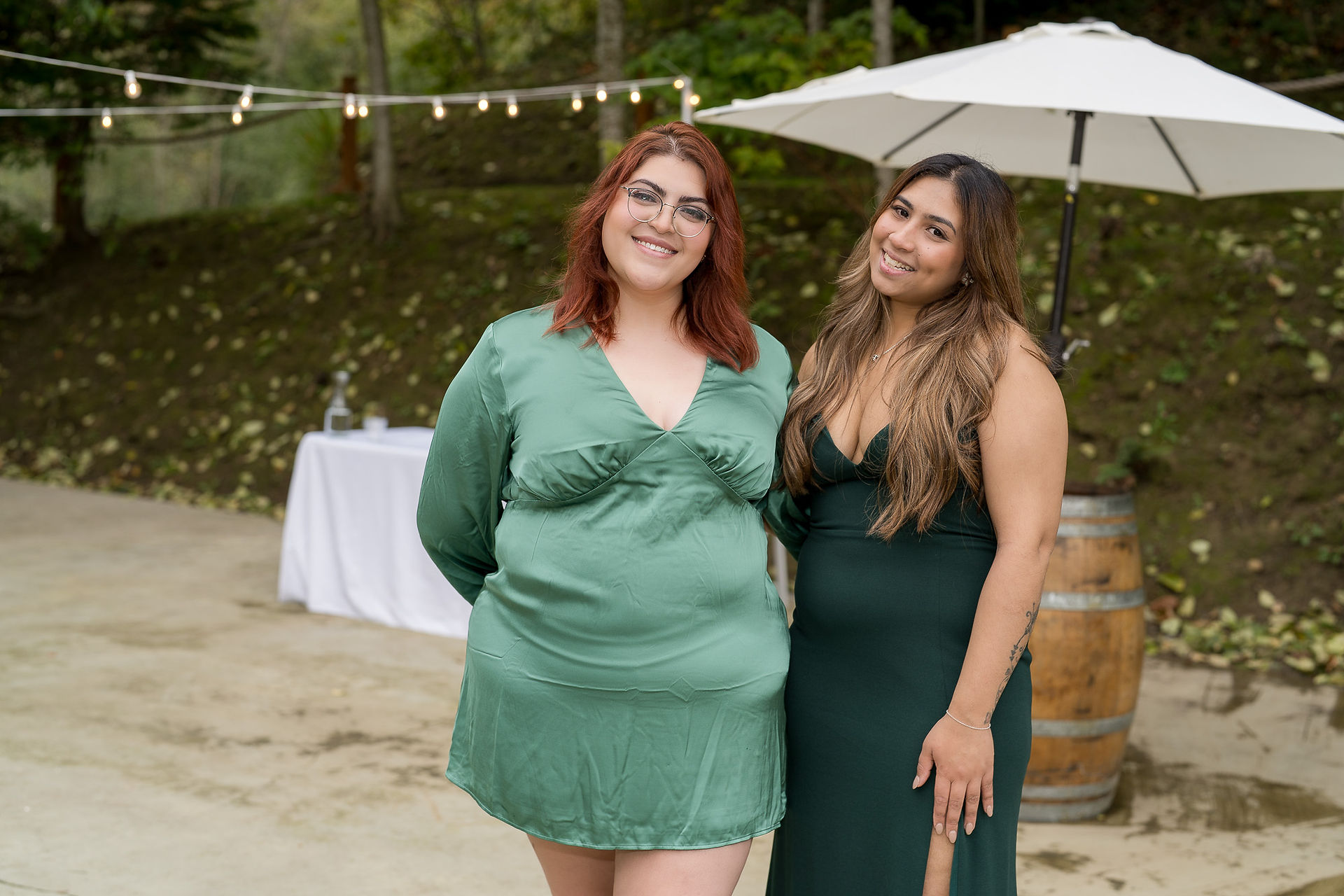 Two smiling women in elegant green dresses at an outdoor wedding event.