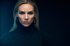 A blond woman in a black turtleneck and hoop earrings. Butterfly light pattern