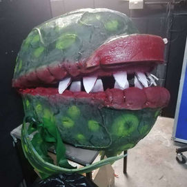 a audrey 2 puppet head designed to be worn by a actor sitting on a table