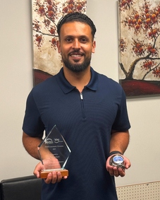 Man smiling, holding a Laudables West award plaque and medal.