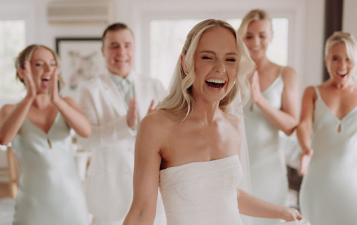 Blonde bride twirling and smiling as guests clap and celebrate in the background