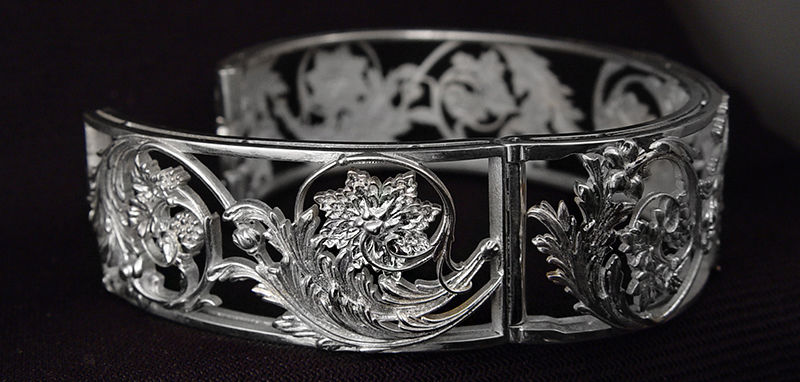 Ornate silver bracelet with detailed floral patterns on a dark background, showcasing intricate craftsmanship and elegant design.
