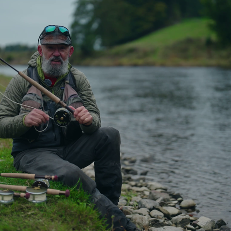 Fly fishing expert sitting by the River Tweed demonstrating rods and reels during Frodin Flies experience day.