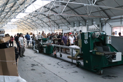 a large group of friends, partners, and community gather in Coastal Sun's greenhouse on the farm which houses machinery to help with farm operations