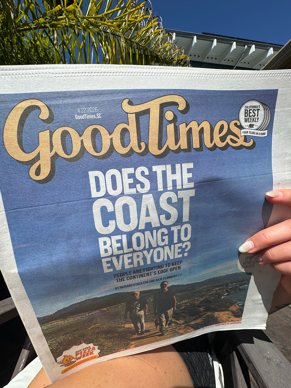 A person with manicured nails holds the Good Times newspaper open with a cover image of people walking on the ocean cliffs along the coastline, and a title that reads "Does the coast belong to everyone?" palm plant in the background