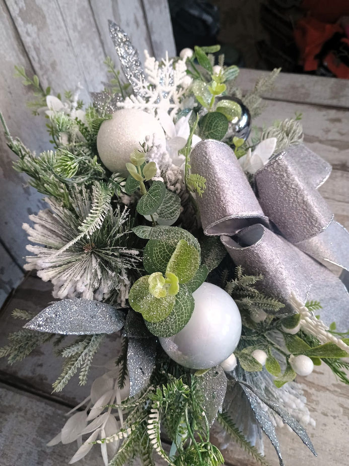 Floral arrangement with white ornaments and silver ribbons on a wooden surface.