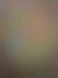 A hanging basket filled with a variety of colorful artificial flowers and green foliage, displayed against a red brick wall