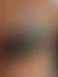 A hanging basket filled with a variety of colorful artificial flowers and green foliage, displayed against a red brick wall