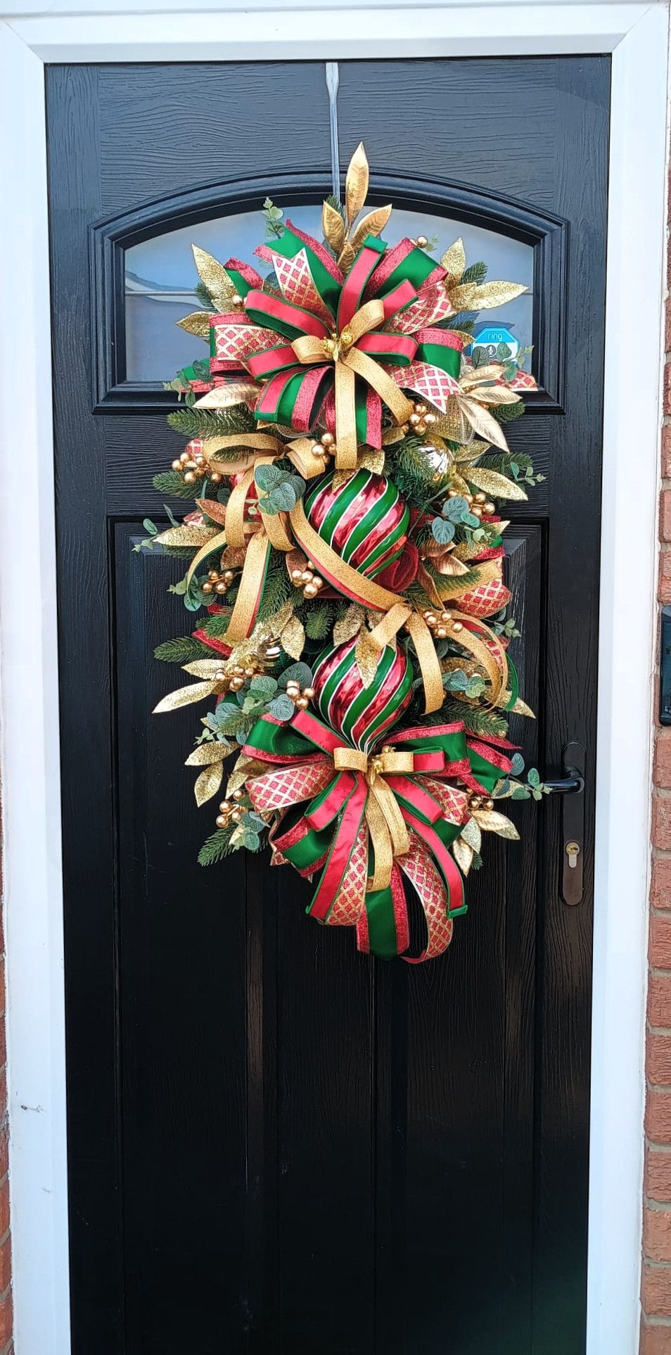 Festive holiday door decoration with red, green, and gold ribbons and ornaments.