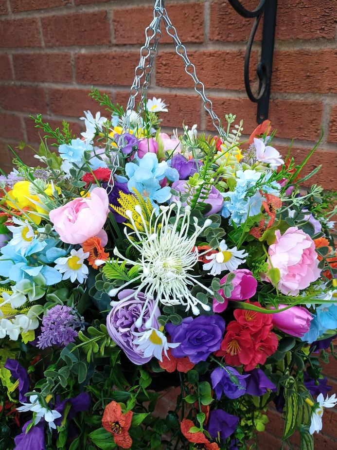 Close up of artificial roses peonies lavender daisies and wildflowers in rainbow hanging baske