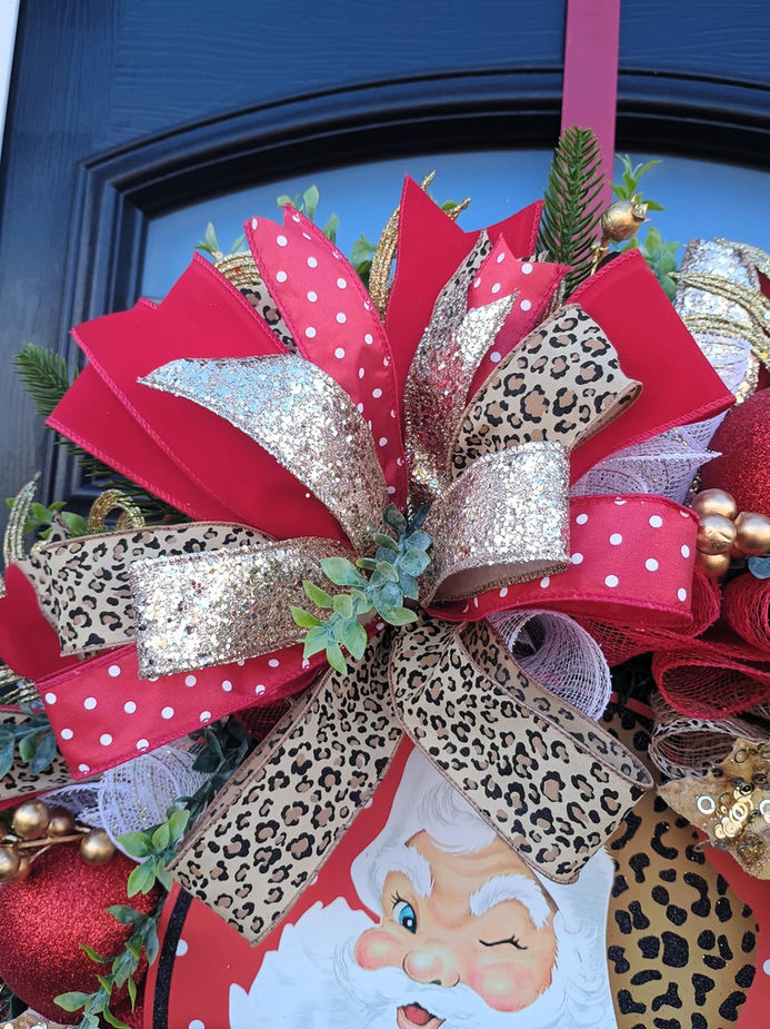 Red and gold bow on a Christmas wreath with a Santa graphic.