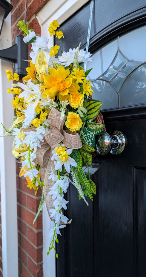 Yellow and white floral door decoration with bow, on a black door frame