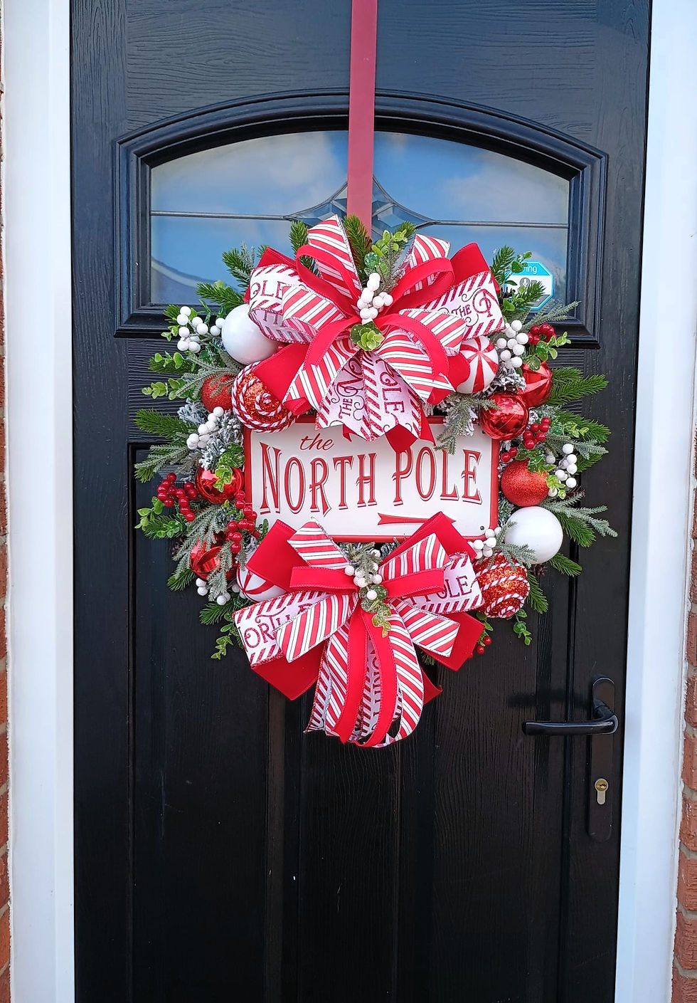 Festive wreath hanging on a black door reading North Pole for Christmas.
