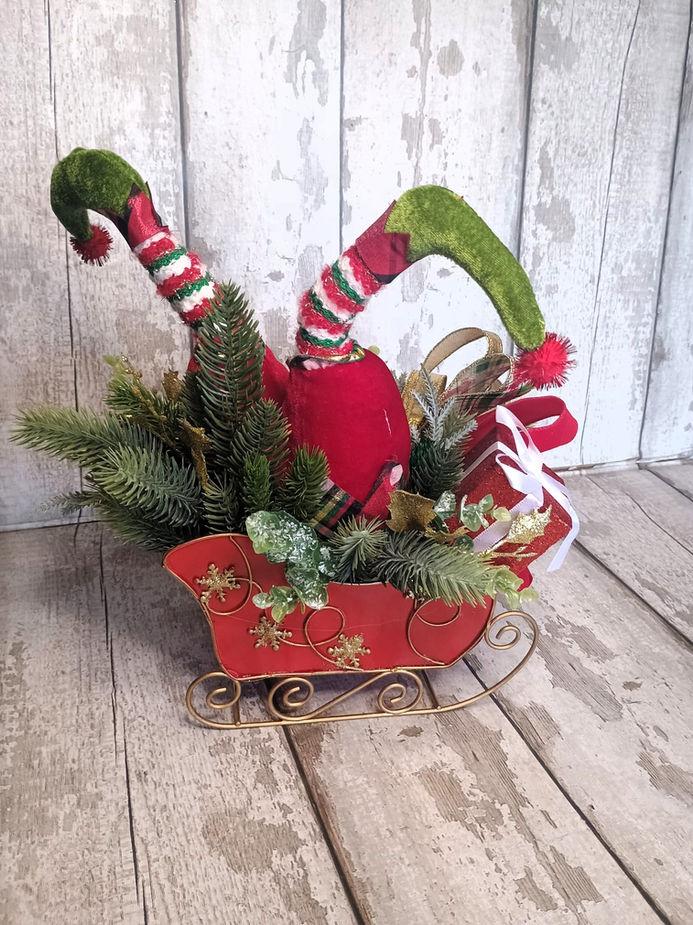 Christmas elf decoration with red sled and green and red striped legs.