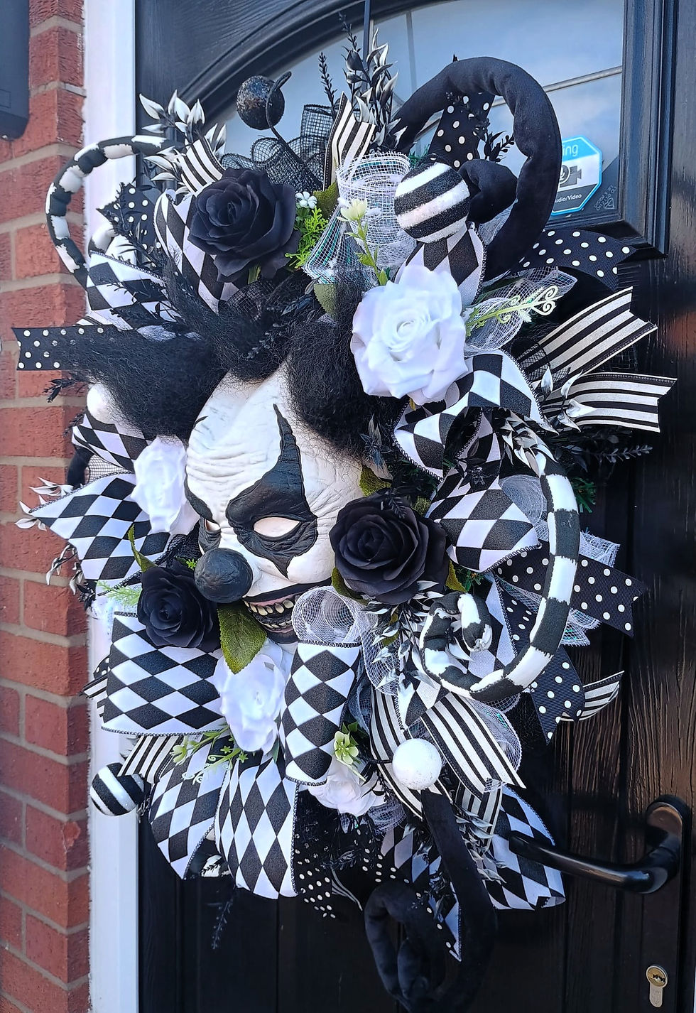 Thumbnail: Clown face mask with black and white ribbons and flowers in decorative wreath