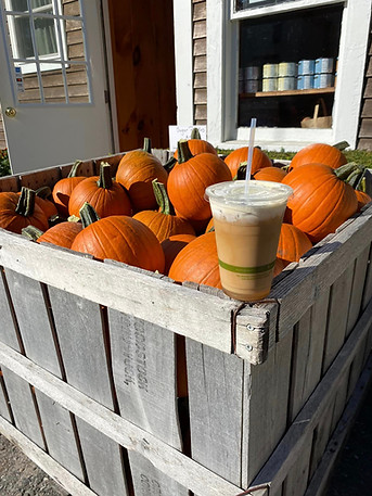 Sugar pumpkins in a crate with an iced coffee on the edge